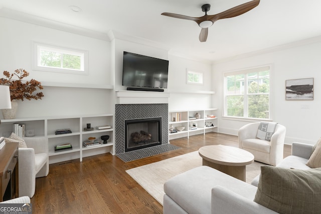 living area with a tiled fireplace, plenty of natural light, ceiling fan, and wood finished floors