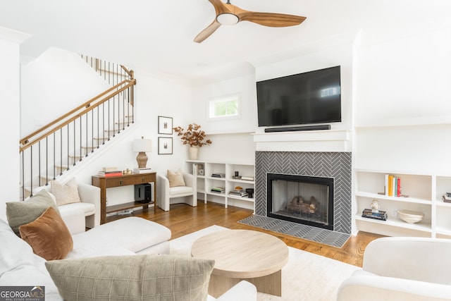 living room with ceiling fan, a tiled fireplace, wood finished floors, and stairway