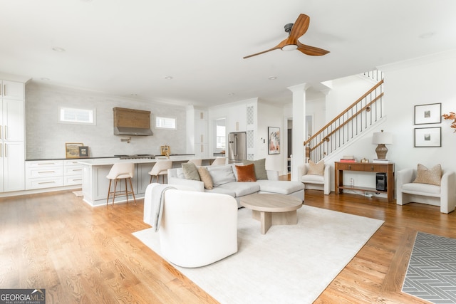 living room with stairway, crown molding, a ceiling fan, and light wood-style flooring