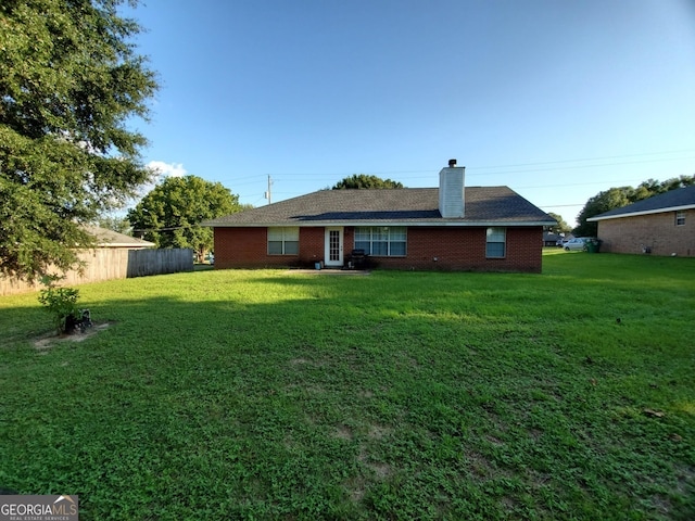 rear view of house featuring a chimney, a yard, and brick siding