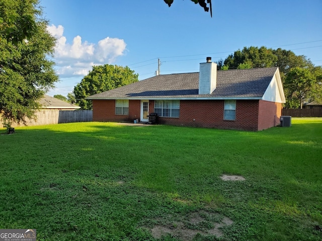 rear view of property featuring fence, brick siding, a chimney, central air condition unit, and a lawn