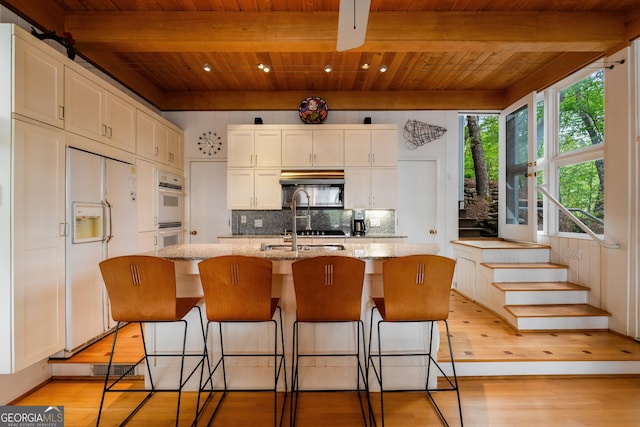 1006 Perrin Cove Rd, Tiger, GA 30576 - kitchen with white appliances, a wood ceiling with exposed beams, light wood-style flooring, an island with sink, and backsplash