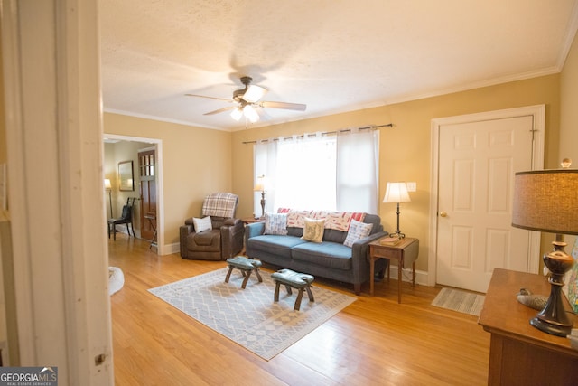 living area featuring crown molding, a ceiling fan, baseboards, and light wood finished floors