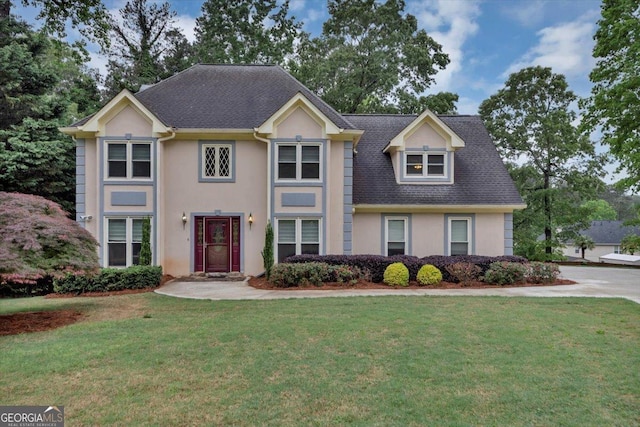 view of front facade featuring roof with shingles, stucco siding, and a front yard