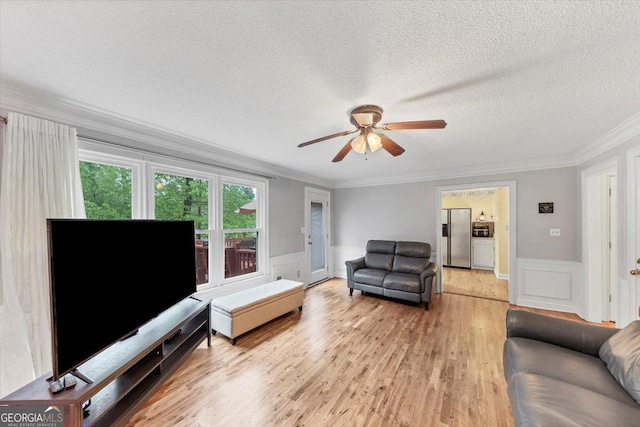 living room featuring ornamental molding, a textured ceiling, ceiling fan, and a decorative wall