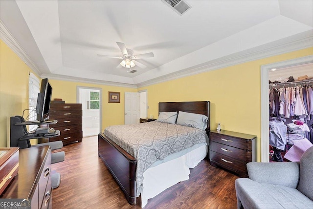 bedroom with a spacious closet, a tray ceiling, dark wood-type flooring, and visible vents