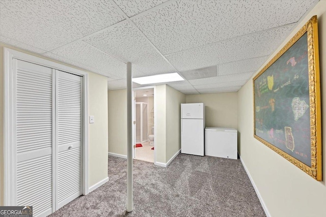 finished below grade area featuring a paneled ceiling, refrigerator, carpet floors, baseboards, and freestanding refrigerator