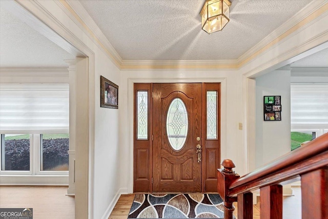 foyer with crown molding, a textured ceiling, baseboards, and wood finished floors