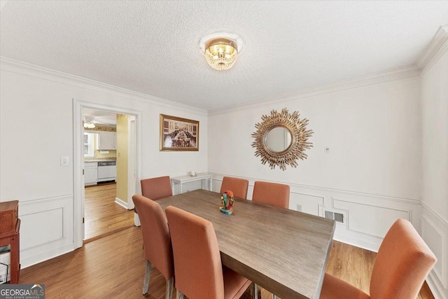 dining area featuring crown molding, a textured ceiling, wood finished floors, and visible vents