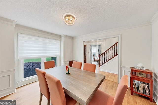 dining space with light wood-type flooring, ornamental molding, a textured ceiling, and stairway