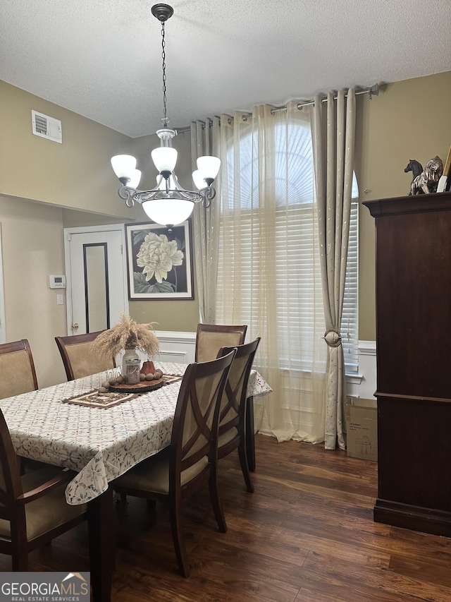 dining room featuring dark wood-style flooring, a textured ceiling, an inviting chandelier, and visible vents