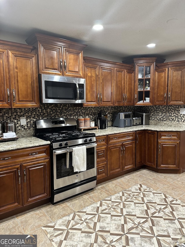 kitchen featuring tasteful backsplash, light stone countertops, glass insert cabinets, stainless steel appliances, and recessed lighting