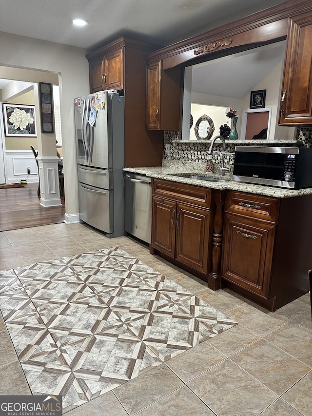 kitchen featuring a sink, light stone counters, decorative backsplash, and stainless steel appliances