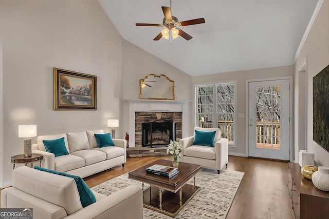 living area with a stone fireplace, a ceiling fan, wood finished floors, and high vaulted ceiling