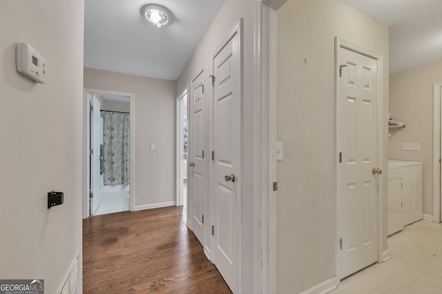 hallway with baseboards, washing machine and dryer, and light wood-type flooring