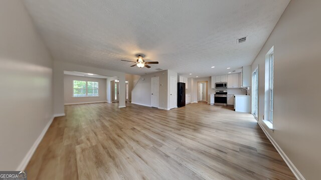8256 Milam Loop, Fairburn, GA 30213 - unfurnished living room featuring visible vents, a ceiling fan, light wood-style floors, and baseboards