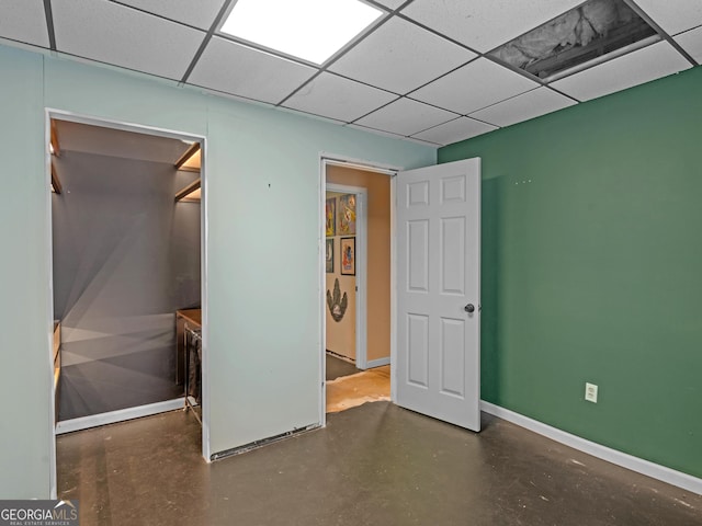 unfurnished bedroom with concrete flooring, baseboards, and a drop ceiling