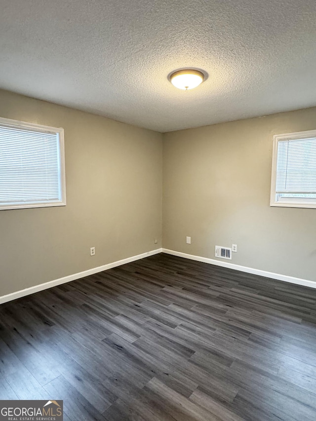 empty room featuring baseboards, dark wood finished floors, a textured ceiling, and visible vents