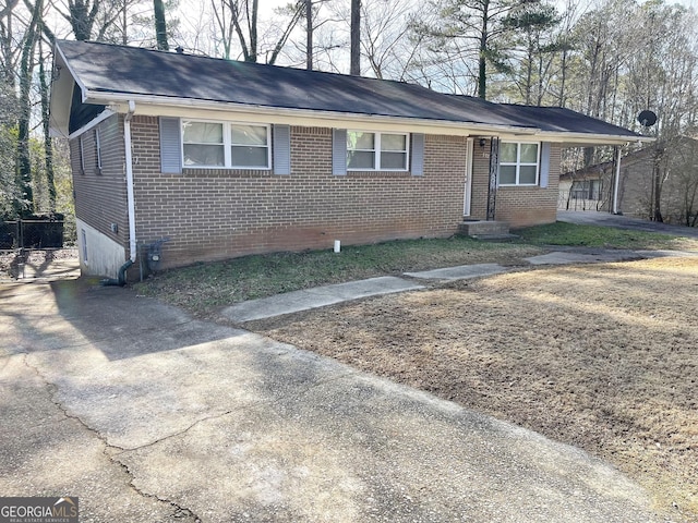 ranch-style house featuring brick siding, a carport, roof with shingles, and aphalt driveway