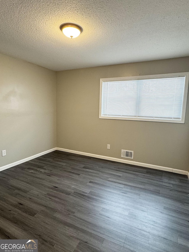 unfurnished room with visible vents, a textured ceiling, dark wood-type flooring, and baseboards