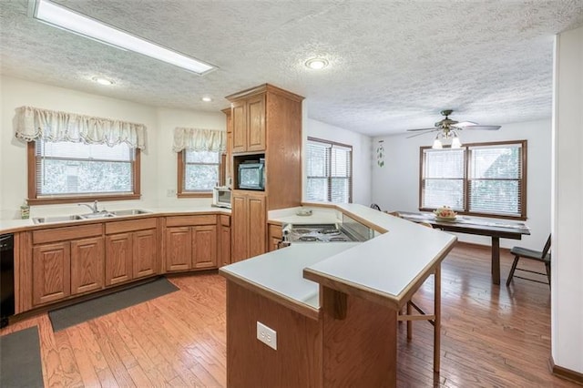 kitchen with a peninsula, a breakfast bar area, light wood-type flooring, a sink, and black appliances