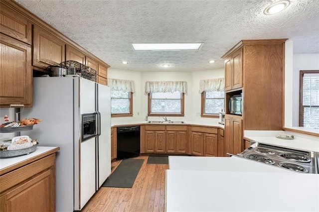 kitchen with a peninsula, light wood-style floors, light countertops, a sink, and black appliances