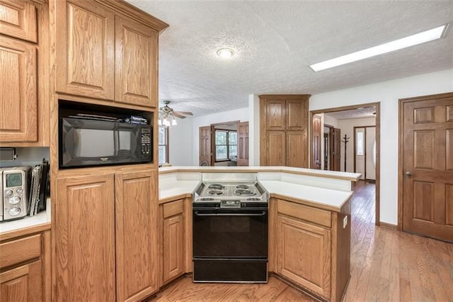kitchen with a textured ceiling, black microwave, electric range oven, light countertops, and a peninsula
