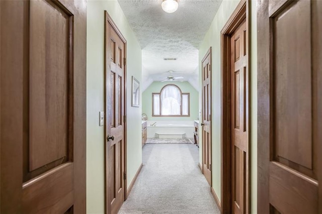 hall featuring visible vents, a textured ceiling, light colored carpet, and vaulted ceiling