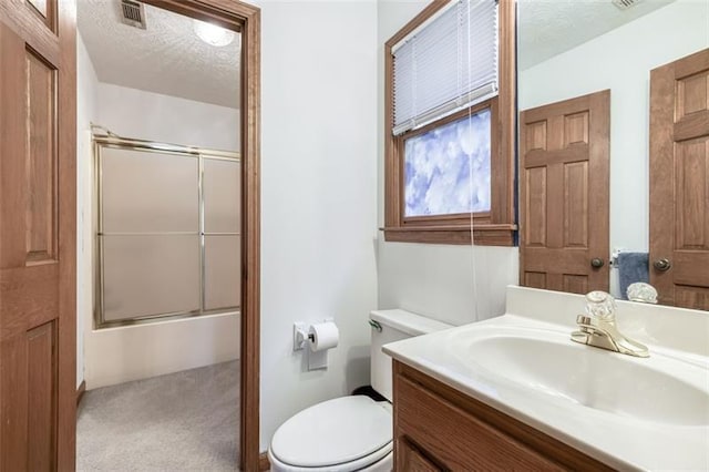 bathroom featuring vanity, visible vents, toilet, bath / shower combo with glass door, and a textured ceiling