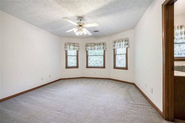 carpeted spare room featuring baseboards, plenty of natural light, a ceiling fan, and visible vents