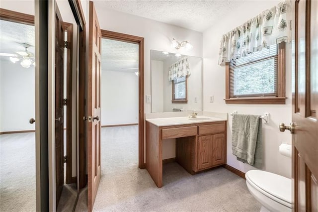 bathroom featuring ceiling fan, vanity, toilet, a textured ceiling, and baseboards