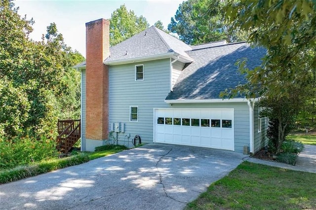 view of home's exterior featuring an attached garage, a shingled roof, driveway, and a chimney