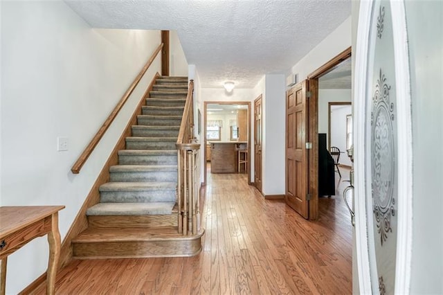 stairs with a textured ceiling, baseboards, and wood finished floors