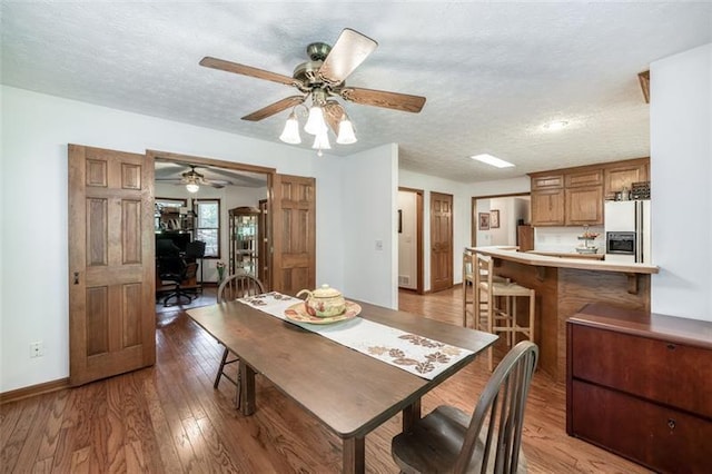 dining space featuring a textured ceiling, ceiling fan, baseboards, and light wood-style floors