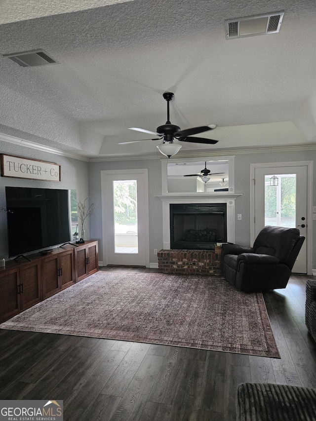 living room featuring a textured ceiling, dark wood finished floors, a healthy amount of sunlight, a tray ceiling, and visible vents