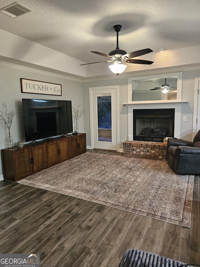 living room with ceiling fan, a brick fireplace, dark wood-style flooring, and visible vents