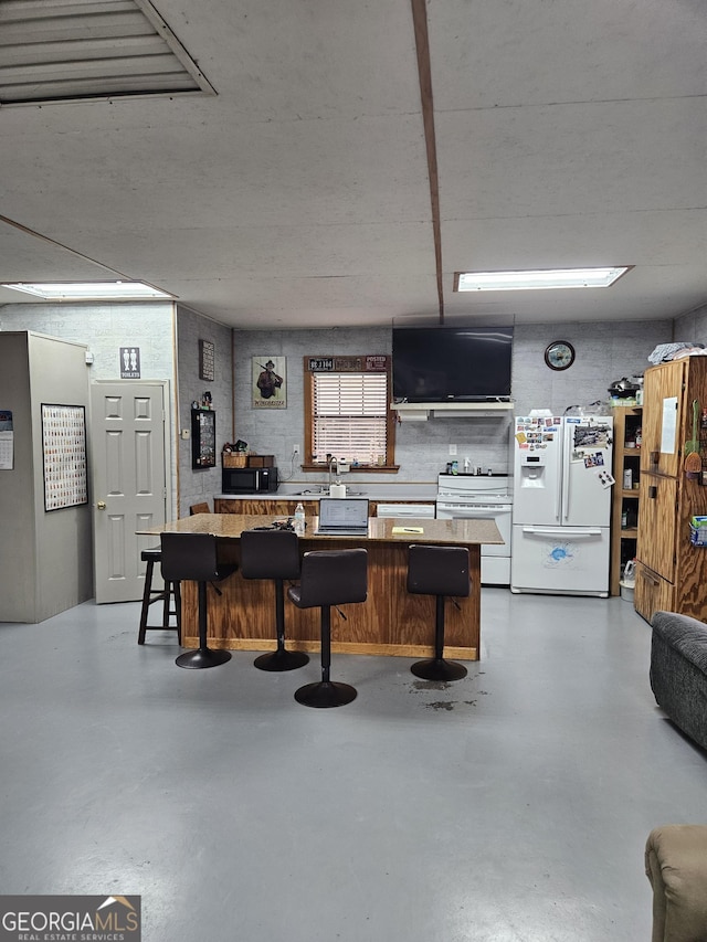 kitchen featuring finished concrete floors, a breakfast bar area, and white appliances
