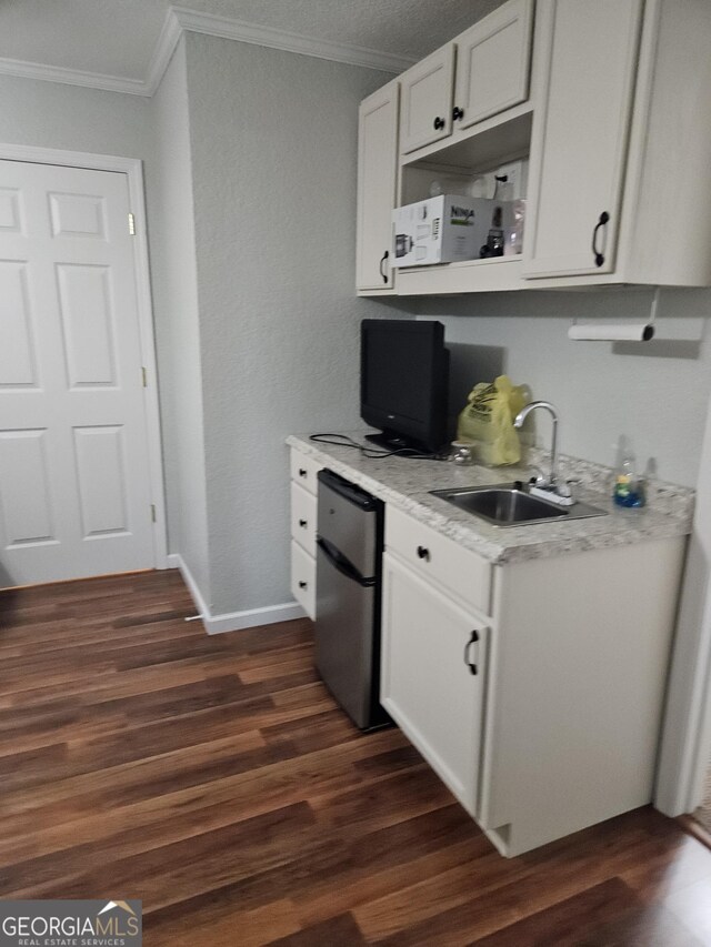 kitchen with ornamental molding, dark wood-style flooring, fridge, light countertops, and a sink