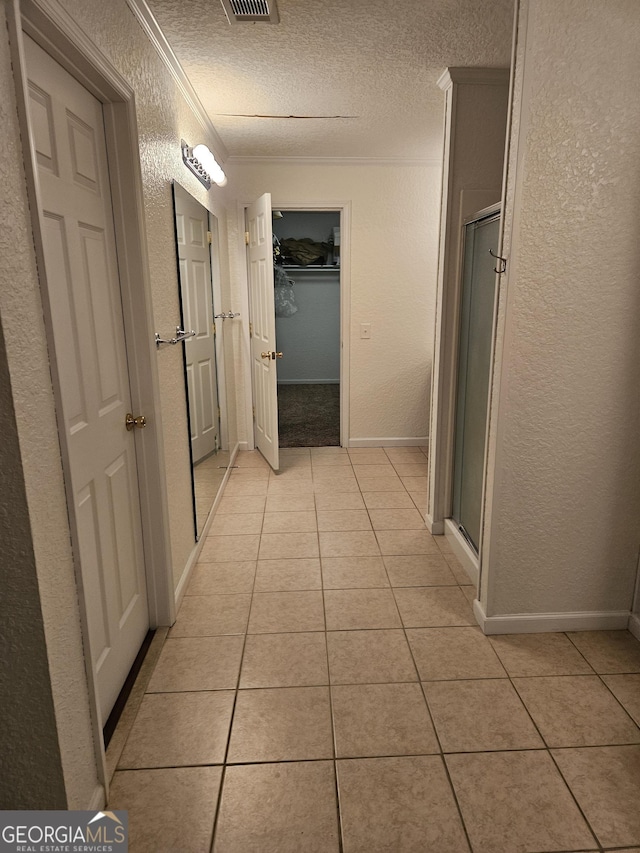 hall with a textured ceiling, a textured wall, visible vents, and light tile patterned floors
