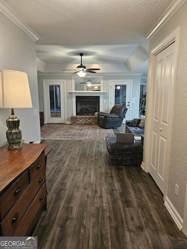 living area with a textured wall, a brick fireplace, dark wood-style floors, a textured ceiling, and a ceiling fan
