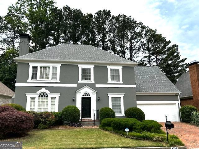 2308 Littlebrooke Dr, Dunwoody, GA 30338 - colonial home featuring stucco siding, a front lawn, an attached garage, and a chimney