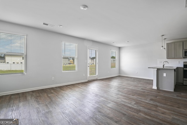 unfurnished living room with visible vents, a sink, dark wood-style flooring, and baseboards