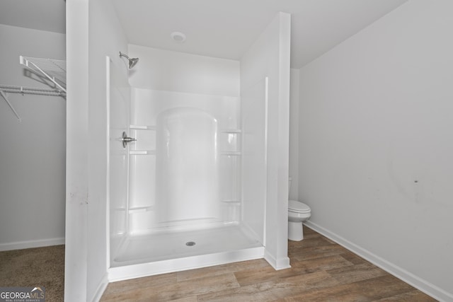 bathroom with baseboards, walk in shower, wood finished floors, and toilet