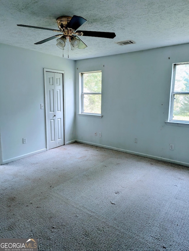 carpeted empty room with baseboards, plenty of natural light, ceiling fan, and visible vents