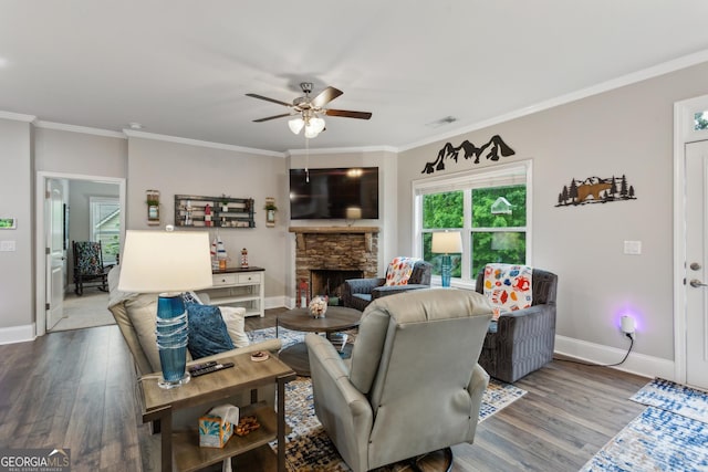 living room featuring a ceiling fan, wood finished floors, baseboards, a stone fireplace, and ornamental molding