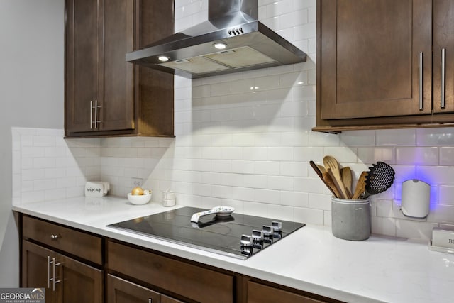 kitchen featuring wall chimney range hood, black electric stovetop, light countertops, tasteful backsplash, and dark brown cabinetry