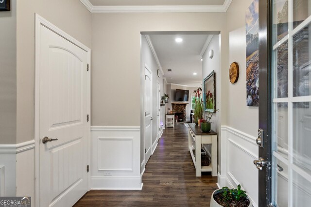 entrance foyer with ornamental molding, dark wood finished floors, wainscoting, and a fireplace