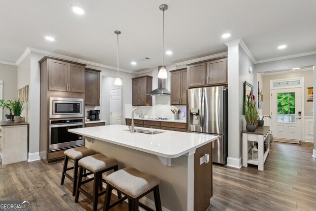 kitchen with stainless steel appliances, wall chimney exhaust hood, a sink, dark wood-style floors, and tasteful backsplash