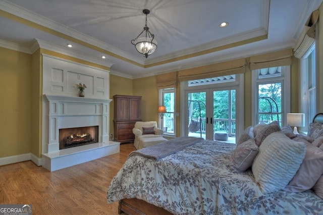 bedroom with ornamental molding, access to exterior, a tray ceiling, french doors, and light wood finished floors
