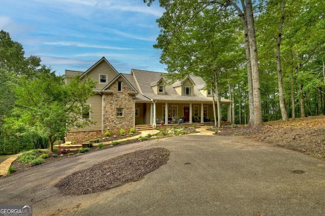 view of front of property featuring covered porch, driveway, and stone siding